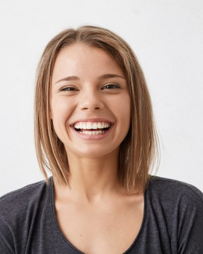 Positive human facial expressions and emotions. Cheerful attractive teenage girl with bob hairstyle grinning broadly, showing her perfect white teeth at camera while spending nice time indoors